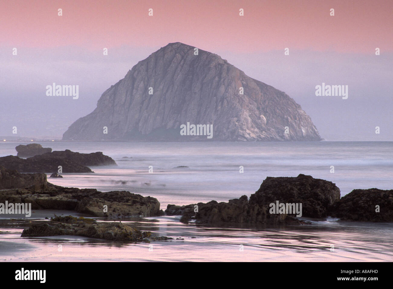 Evening light over Morro Rock ocean waves and fog from Morro Strand State Beach near Morro Bay California Stock Photo