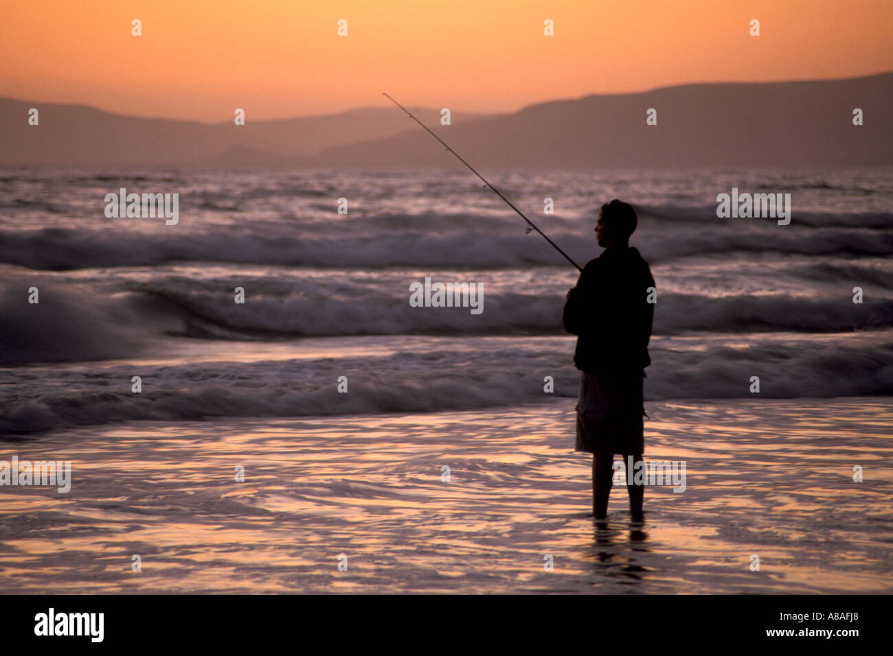 Young man surf fishing in coastal waves at sunset Morro Strand State Beach near Cayucos and Morro Bay California Stock Photo