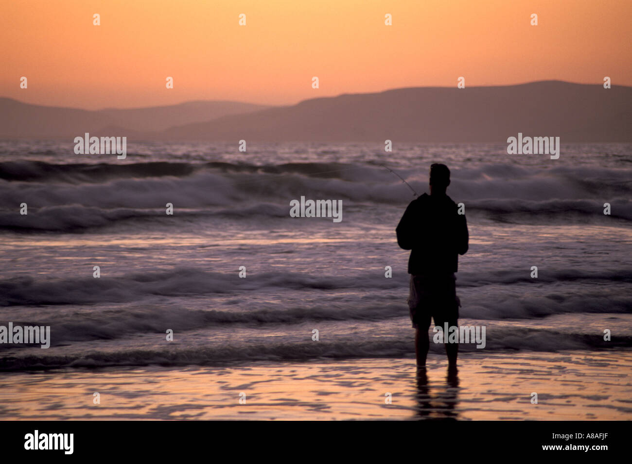 Young man surf fishing in coastal waves at sunset Morro Strand State Beach near Cayucos and Morro Bay California Stock Photo