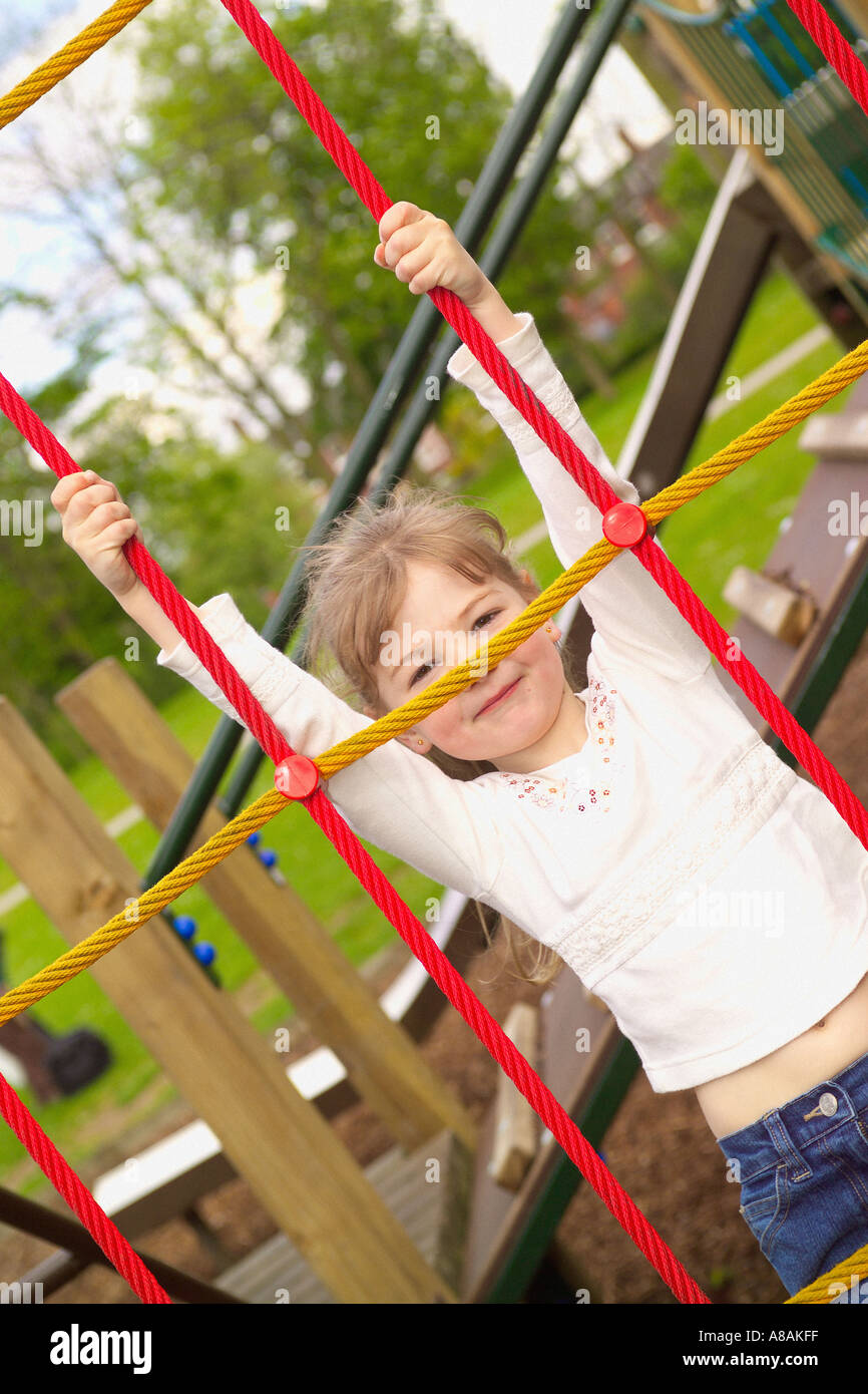 Caucasian child with blonde hair, climbing on a red and yellow scramble net, smiling Stock Photo