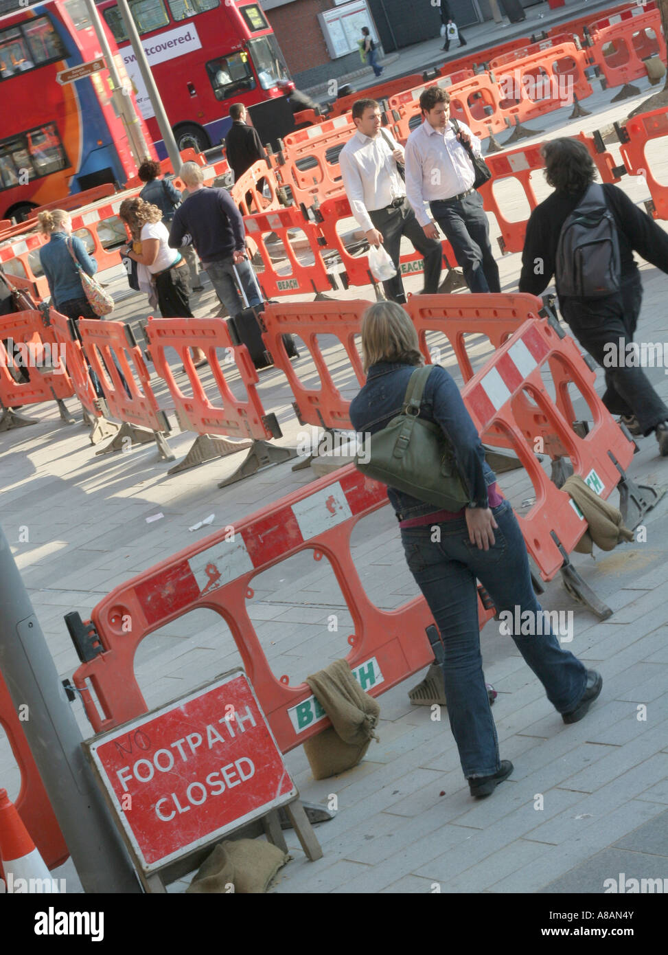 pedestrians walk past construction site on pavement. Stock Photo