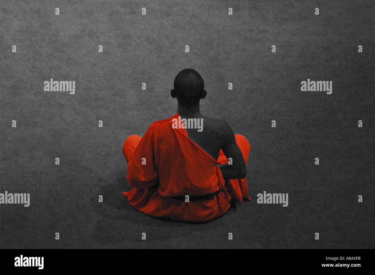 Monochrome image of Buddhist monk sitting in meditation with his orange robe selectively highlighted Stock Photo