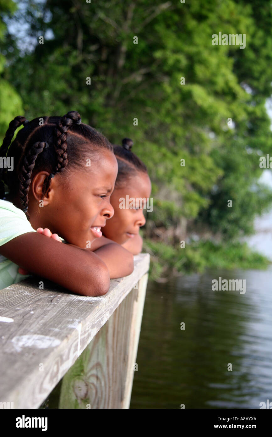 Two Afro American young girls leaning on the railing of the dock observing nature. Stock Photo