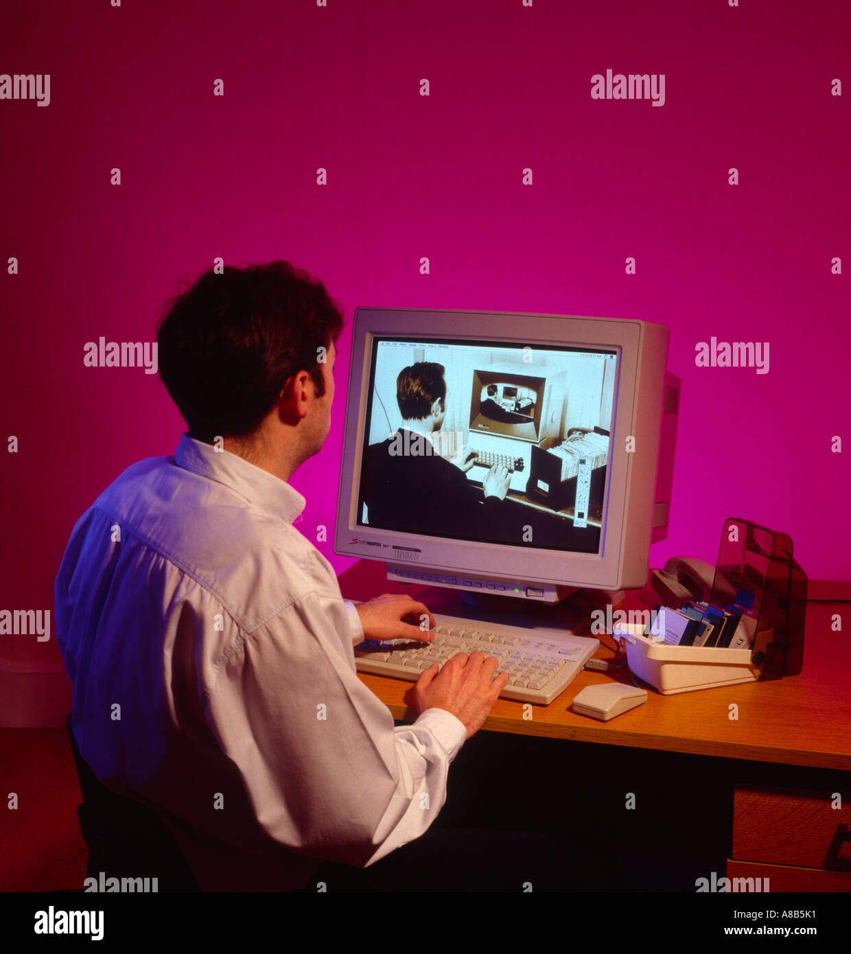 Man at computer looking into the past on his desktop personal computer in 1990s Stock Photo