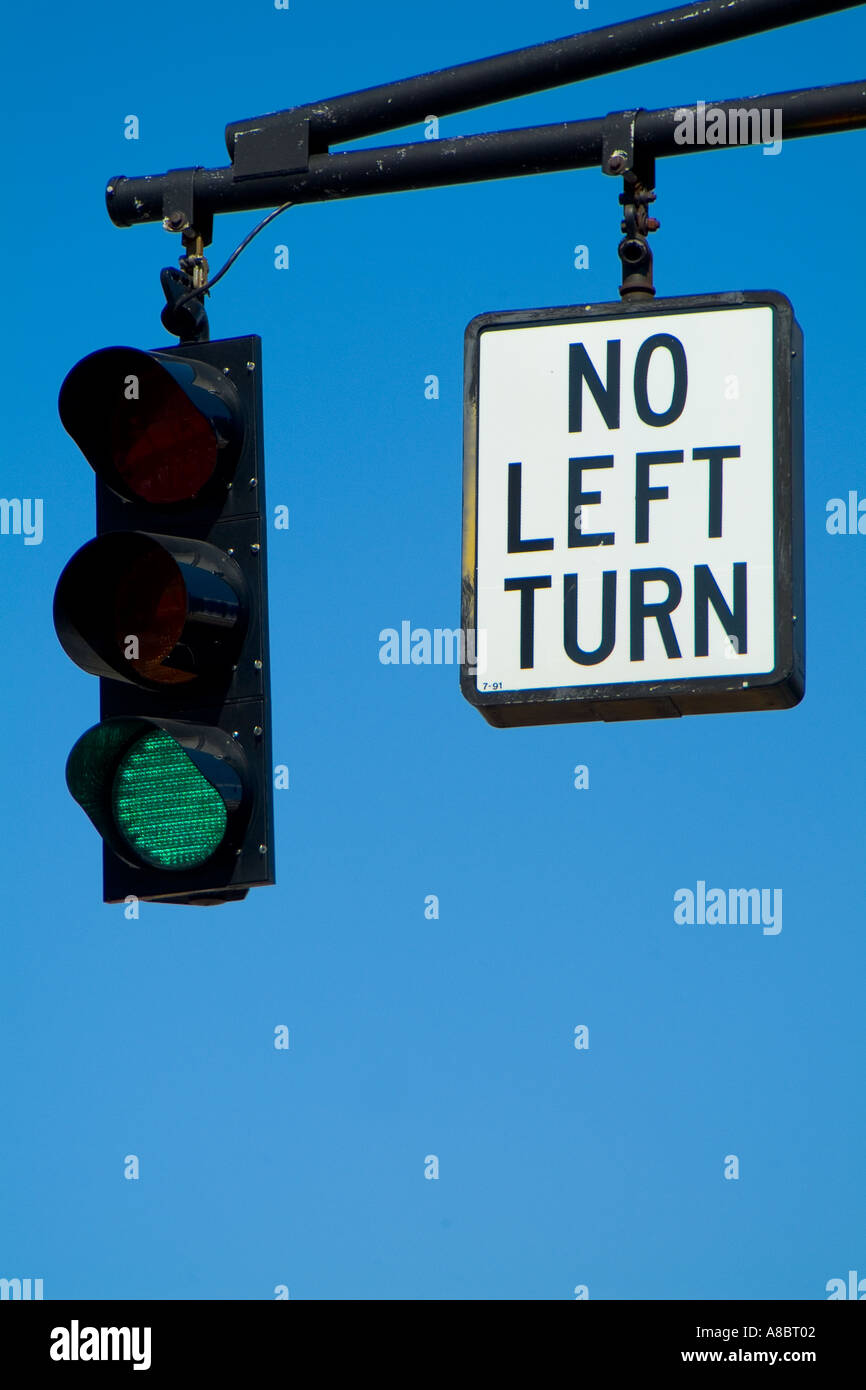 Traffic signal with green light and NO LEFT TURN sign hanging from pole against blue sky Stock Photo