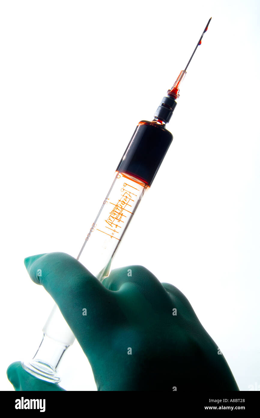Hand in surgical glove holding large syringe and droplet of liquid
