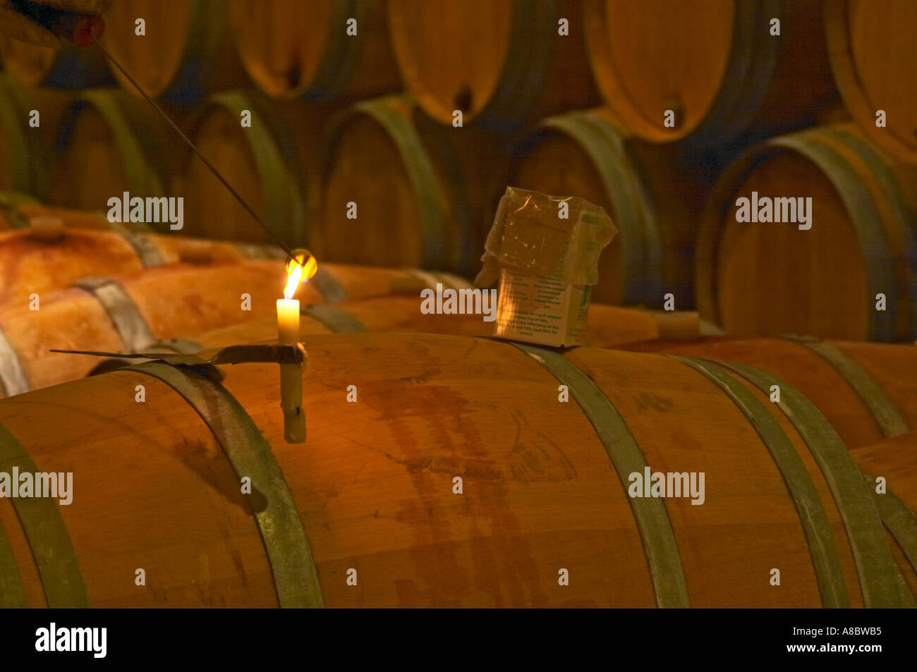 The winery, barrel aging cellar: a burning candle, a box of sulphur pellets and a winery worker lighting a pellet of sulphur to Stock Photo