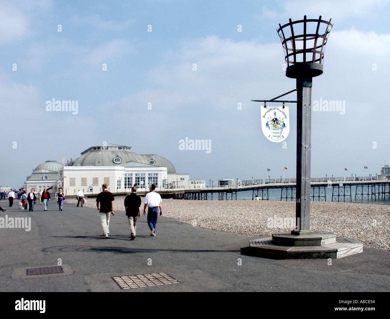 Worthing holiday and seaside resort with people walking esplanade &  town sign fixed to fire beacon with pleasure pier beyond West Sussex England UK Stock Photo