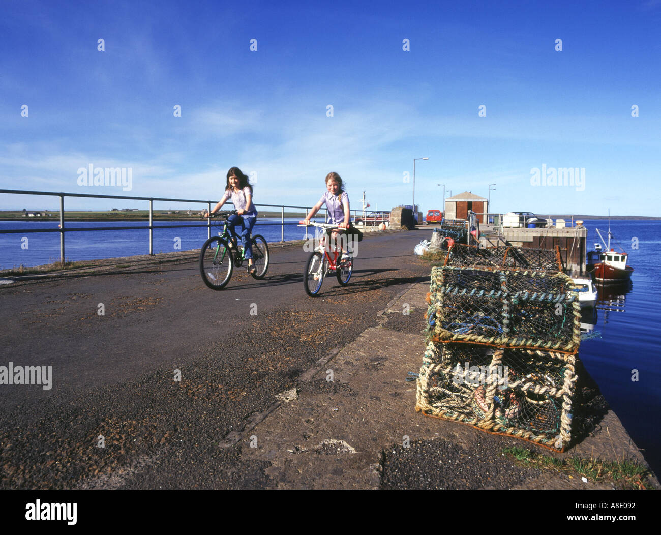 dh Longhope HOY ORKNEY Children riding bicycles on South Ness pier outdoor uk kids cycling child two girls cycle 2 young people Scotland Stock Photo