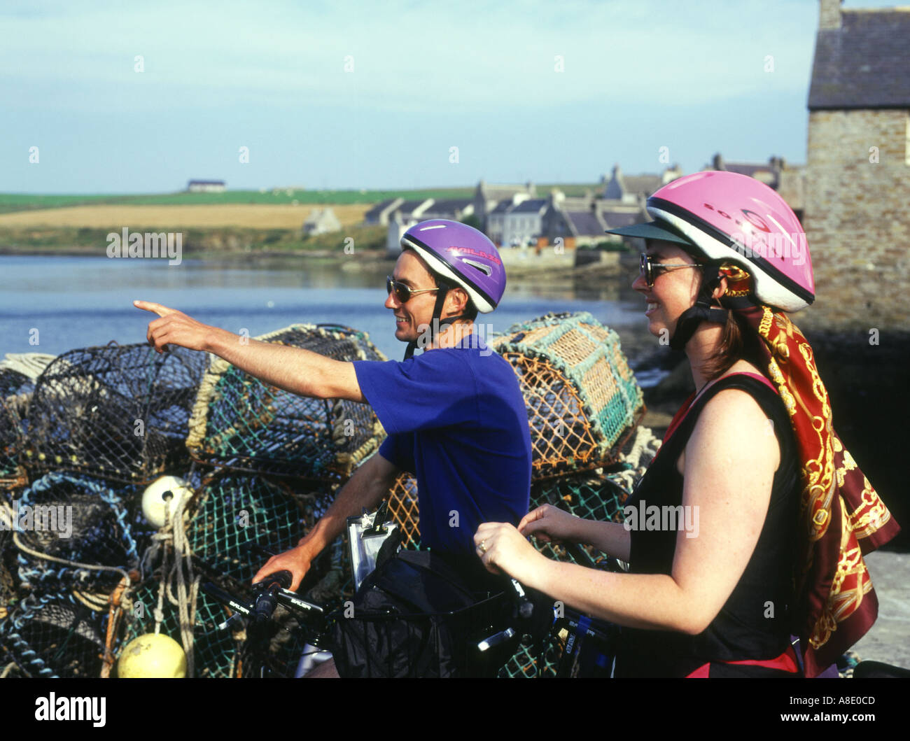 dh Two cyclists holiday ORKNEY Cyclist helmet uk tourist cycle helmets scotland couple cycling sightseeing looking sight seeing bikes pointing bike Stock Photo