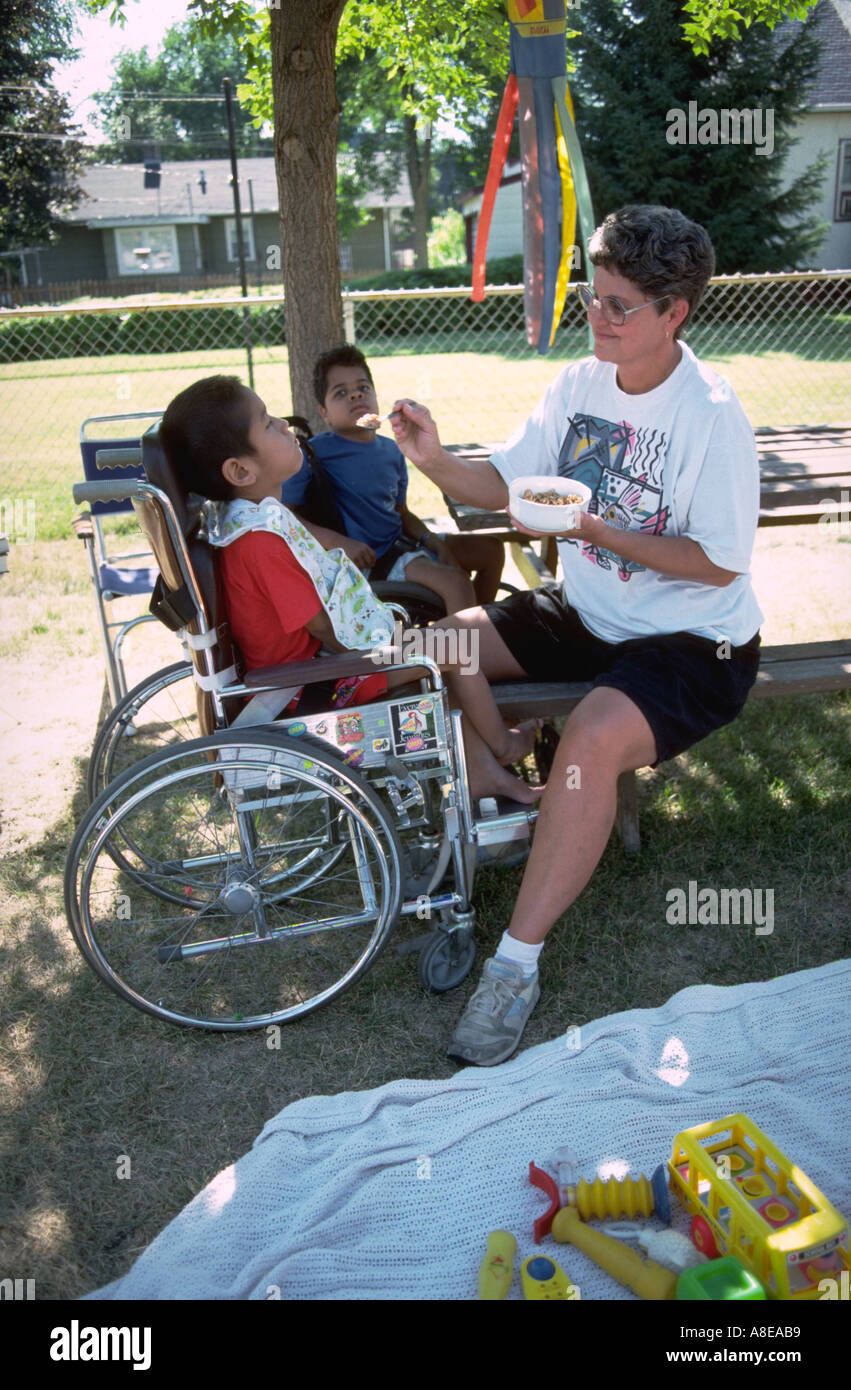 Foster mom feeding disabled kids in wheelchairs age 42 and 8 Stock