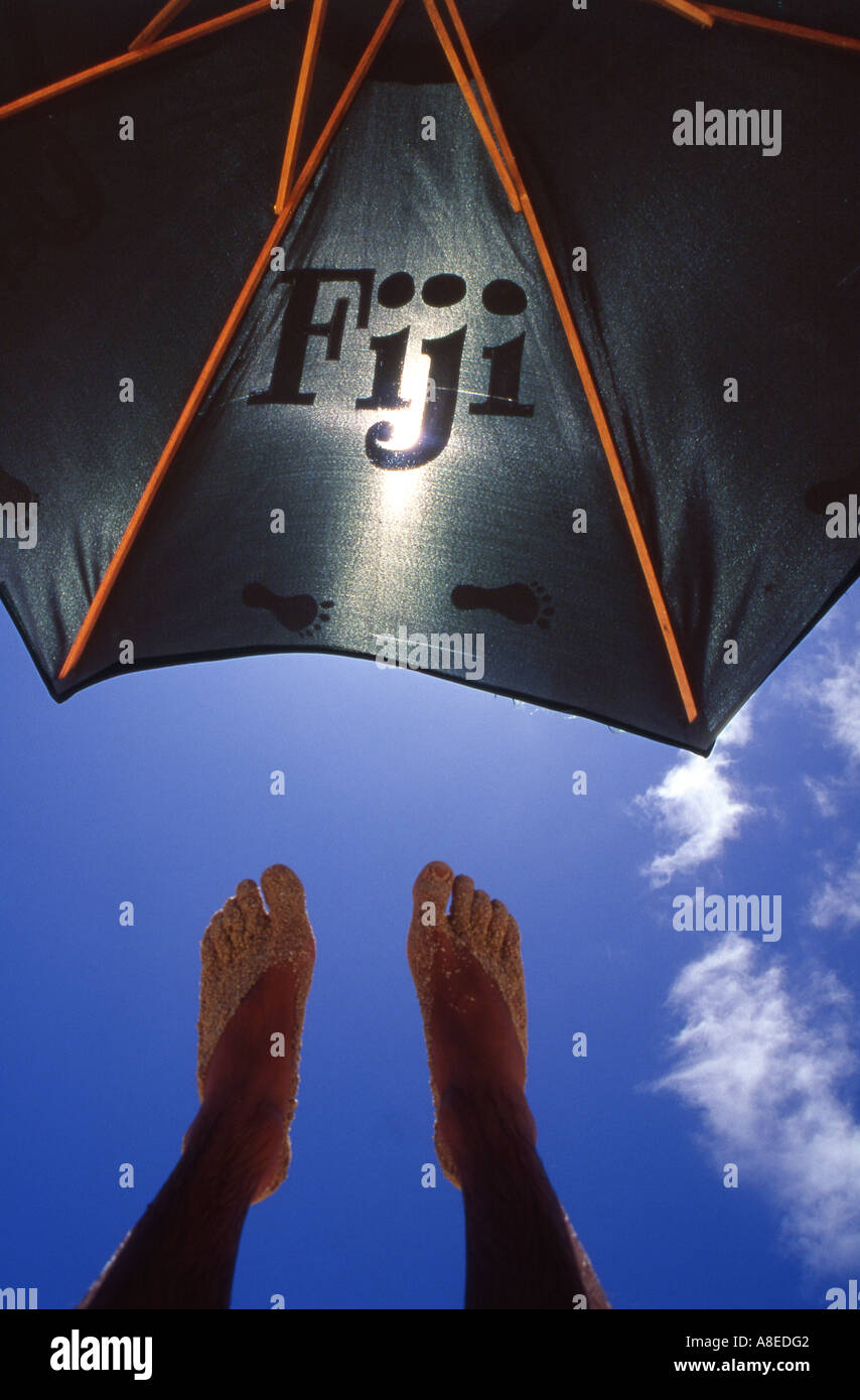 Sandy feet in the shade of a sun umbrella on a beachcomber Island Beach Stock Photo