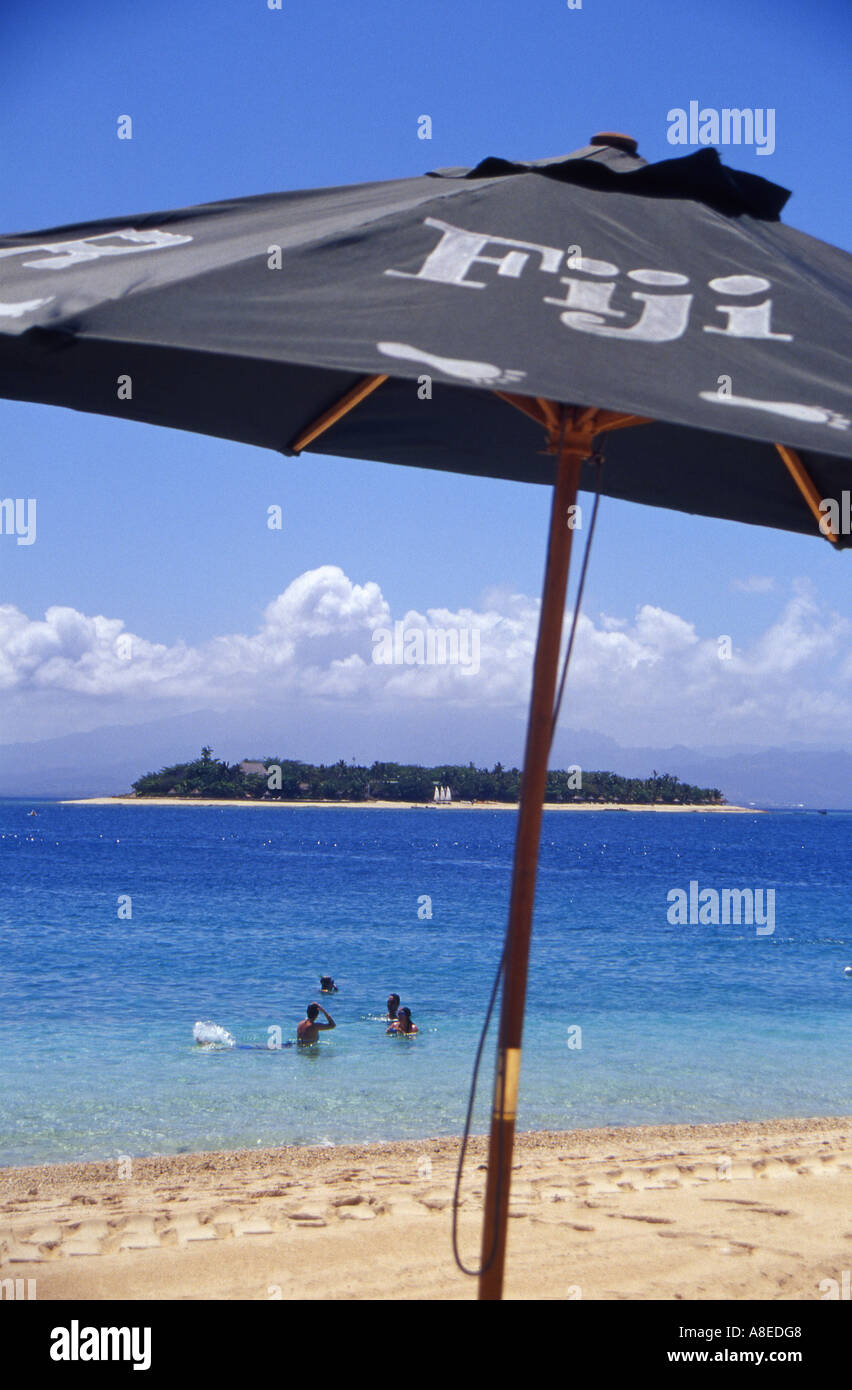View from under a sun umbrella on a beachcomber Island Beach in fiji out towards holiday makers swimming in the sea Stock Photo