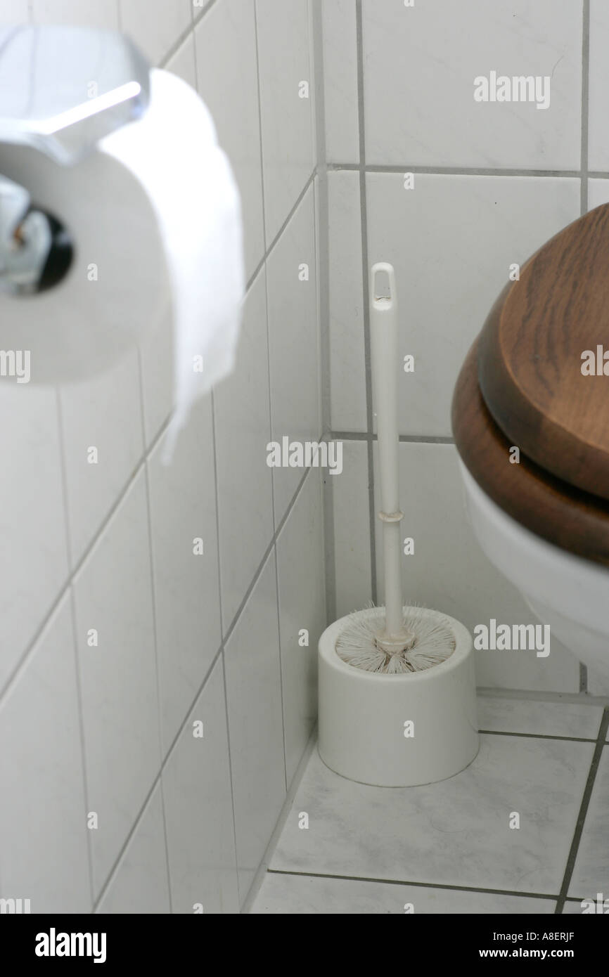 Toilet brush in a corner with toilet bowl and toilet paper roll. Stock Photo
