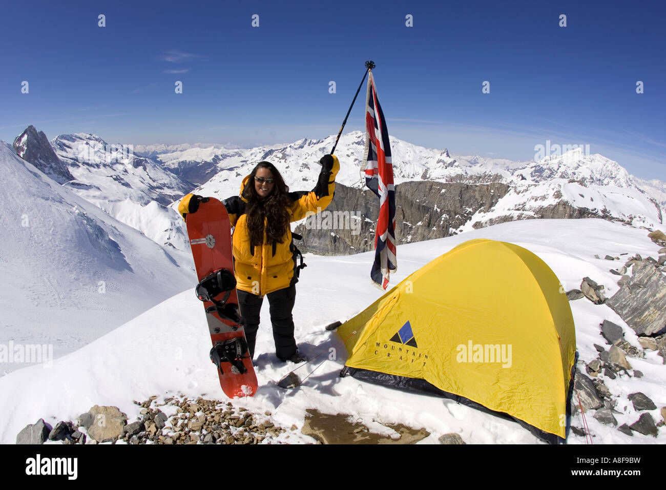 Female Mountaineer on summit of mountain with Union Jack and Snowboard