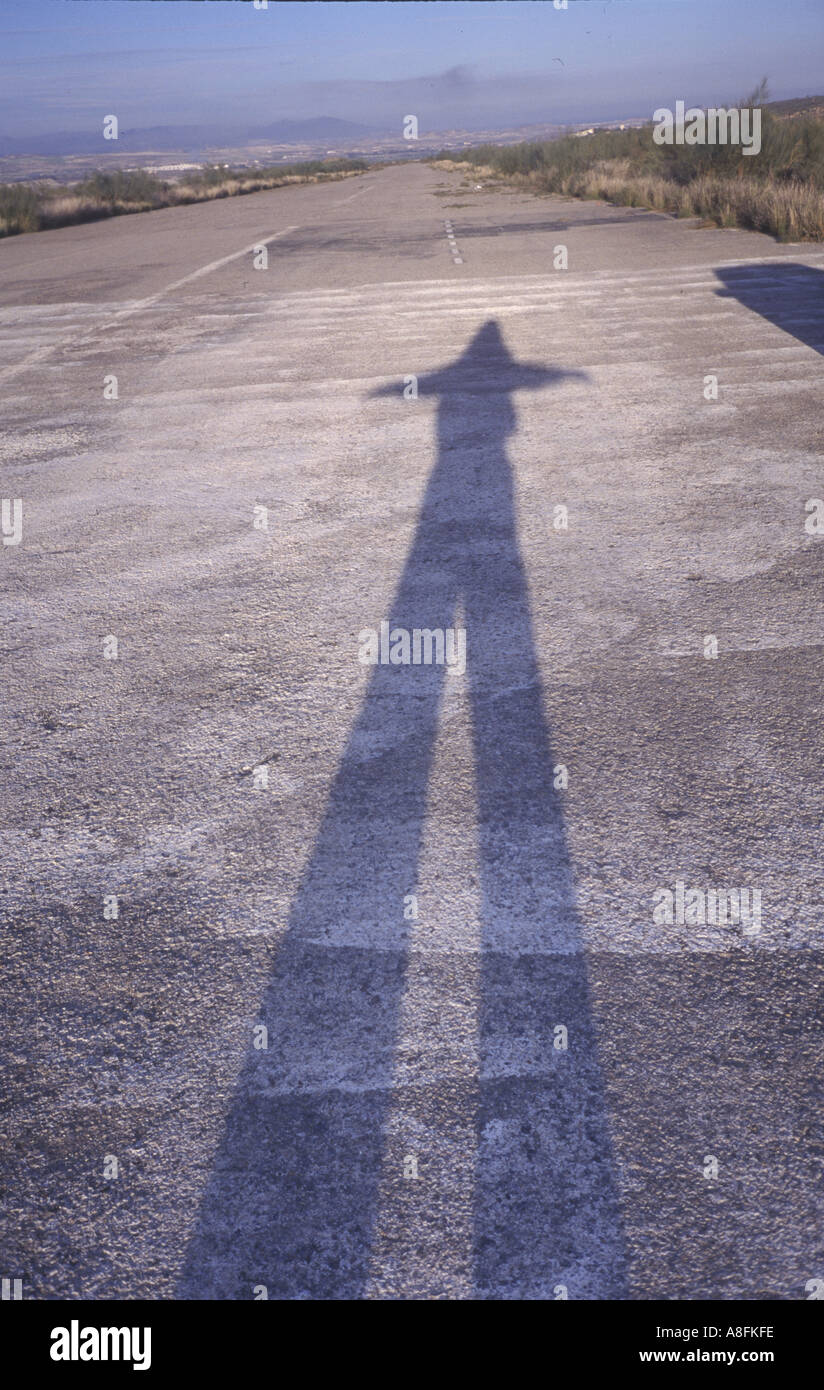 shadow of man with arms outstretched imitating wings on disused airport runway Stock Photo