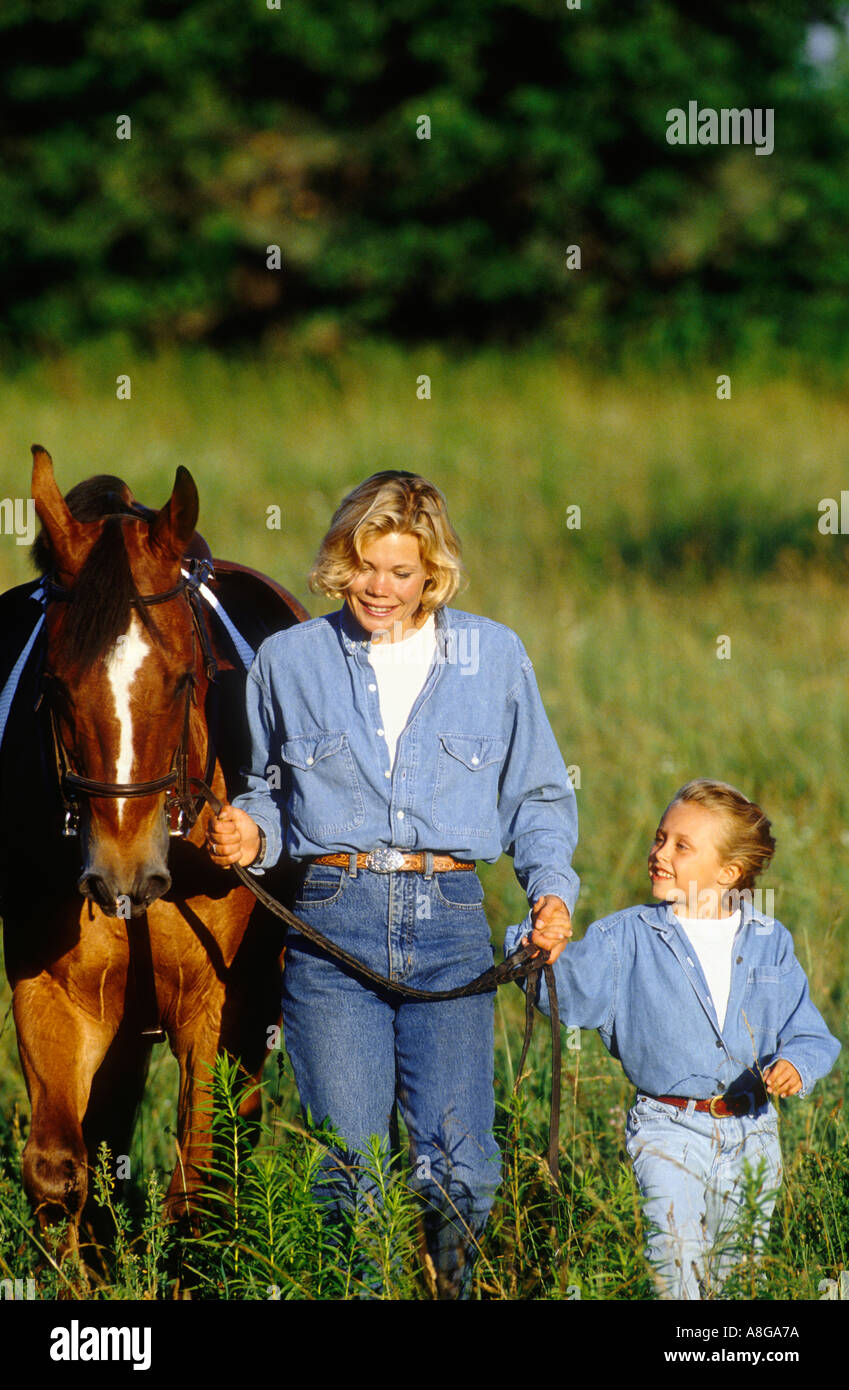 mother and daughter walking in field with horse Stock Photo