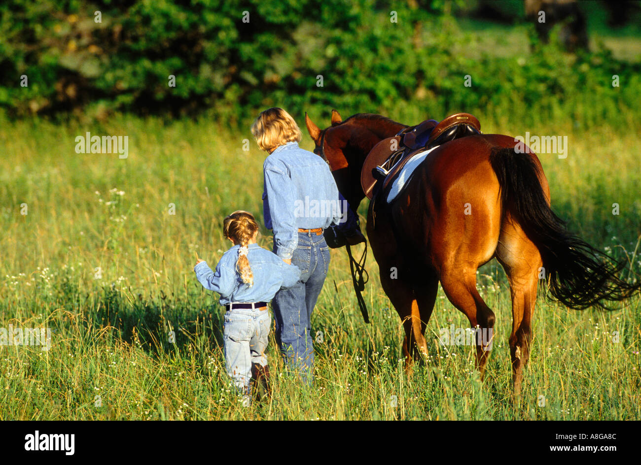 mother daughter walking with horse in field Stock Photo