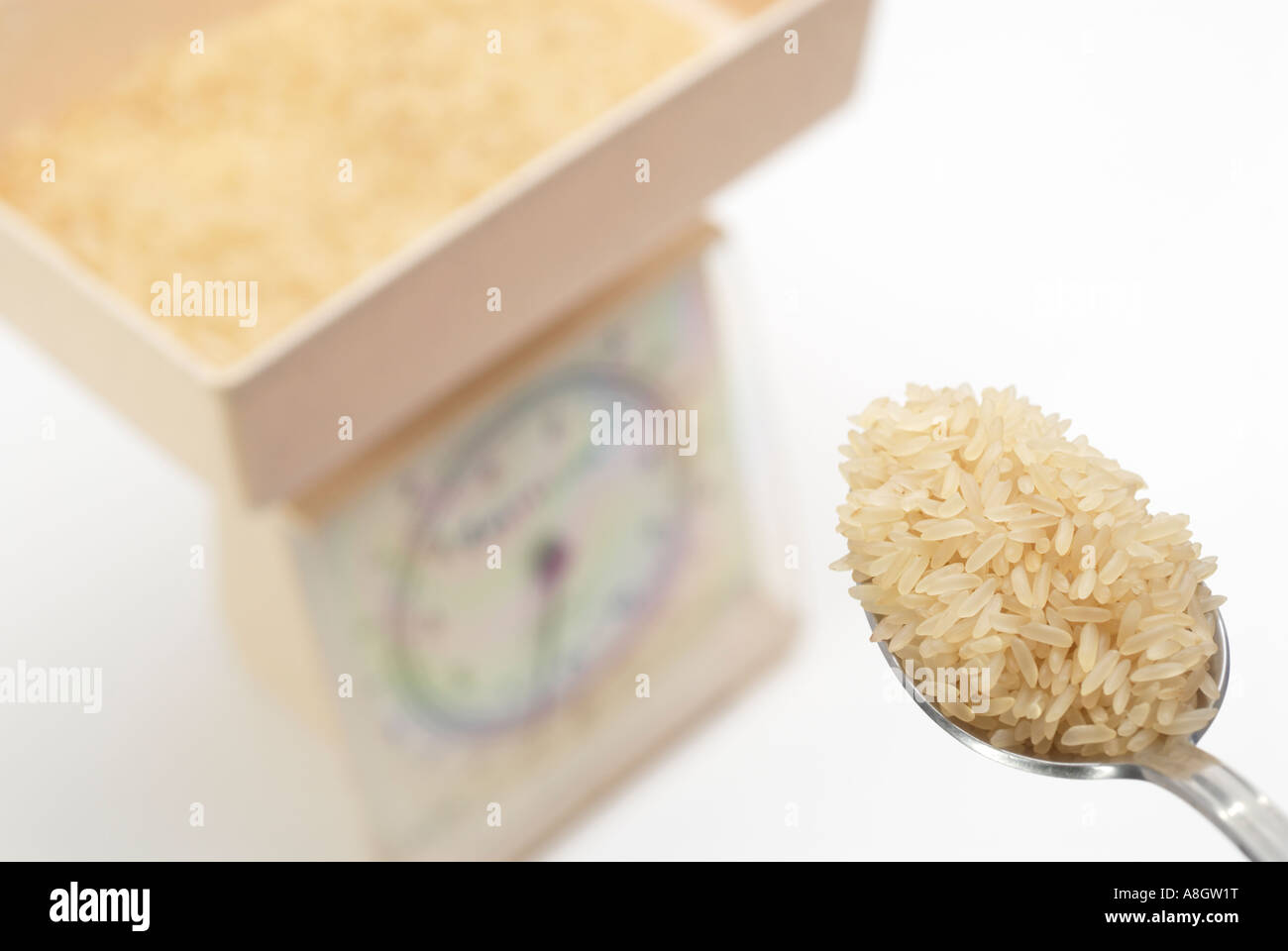Heaped tablespoon of long grained rice being placed on kitchen scales for weighing Stock Photo