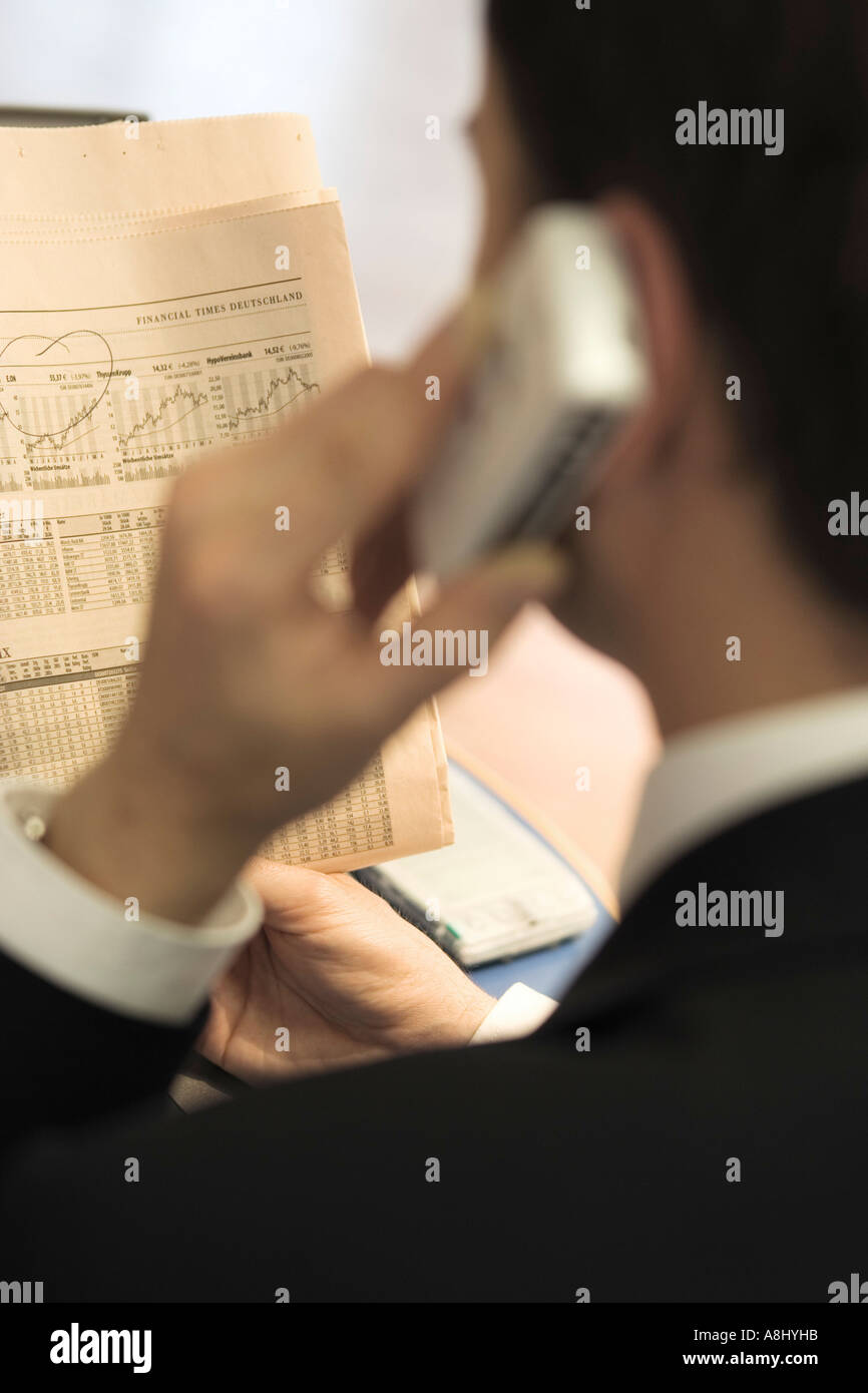 Business man from the back view with the telefon in the left hand side reading a stock market newspaper Stock Photo