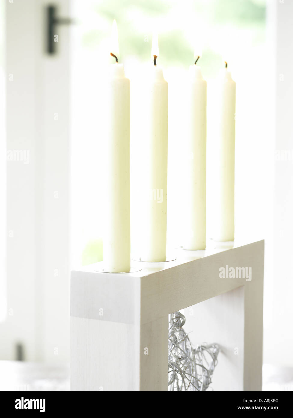 line of four white candles in wooden holder against window Stock Photo