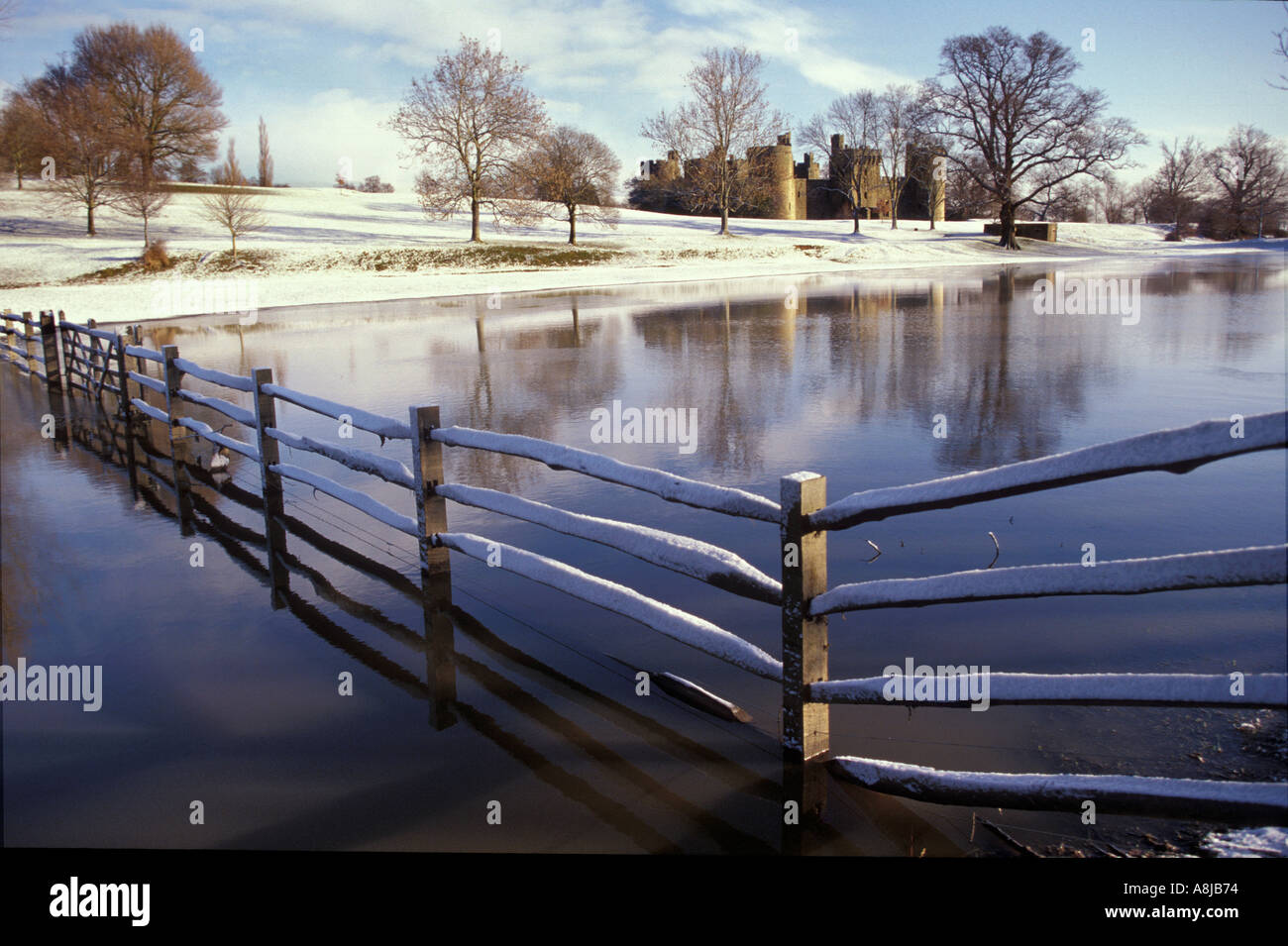 Flooded fields reflecting winter landscape with lfence and snow around Bodiam Castle in East Sussex UK Stock Photo