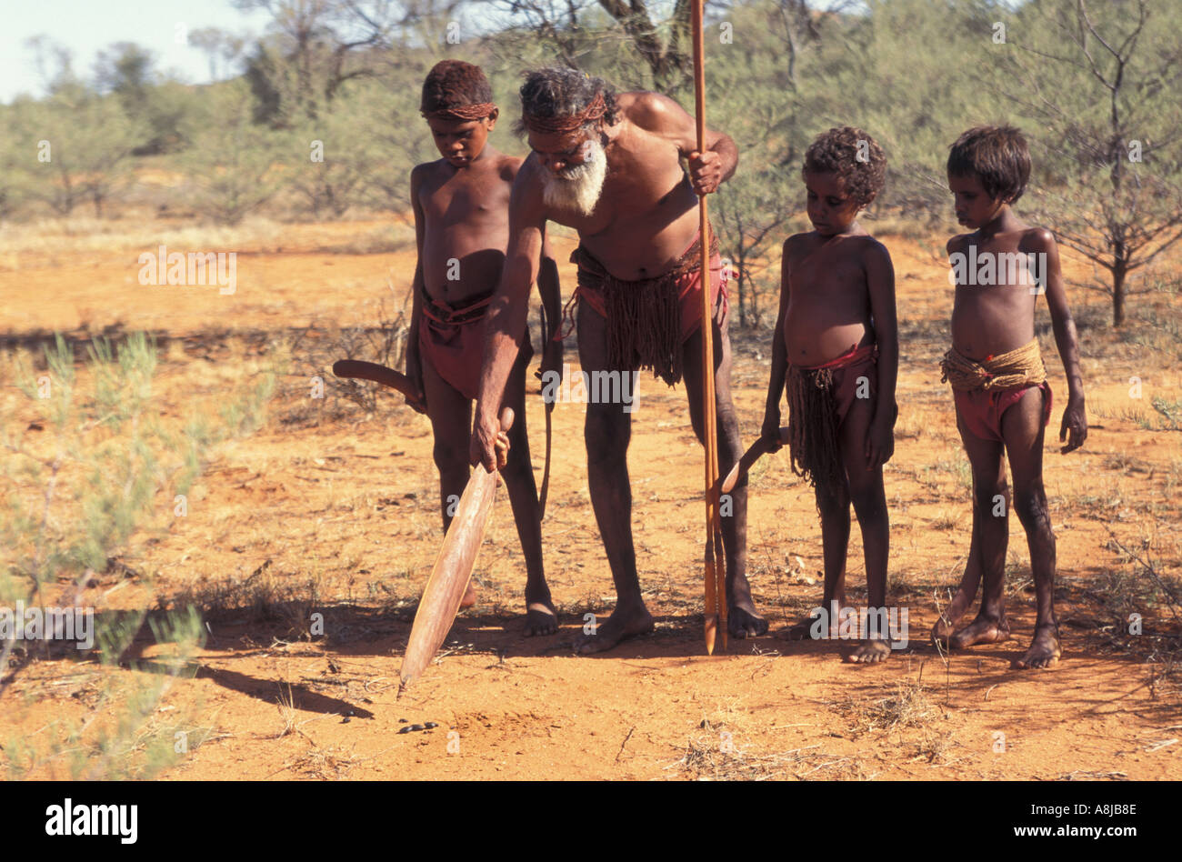 Aboriginal elder points to track in desert sand with spear in teaching boys to hunt Central Australia Stock Photo