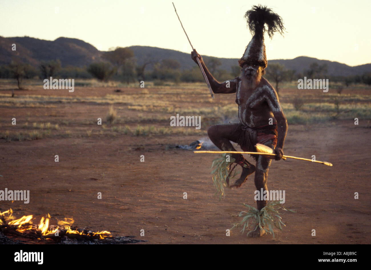 Aboriginal elder in traditional decoration dances beside a fire with spear and boomerang at dusk in the desert Central Australia Stock Photo