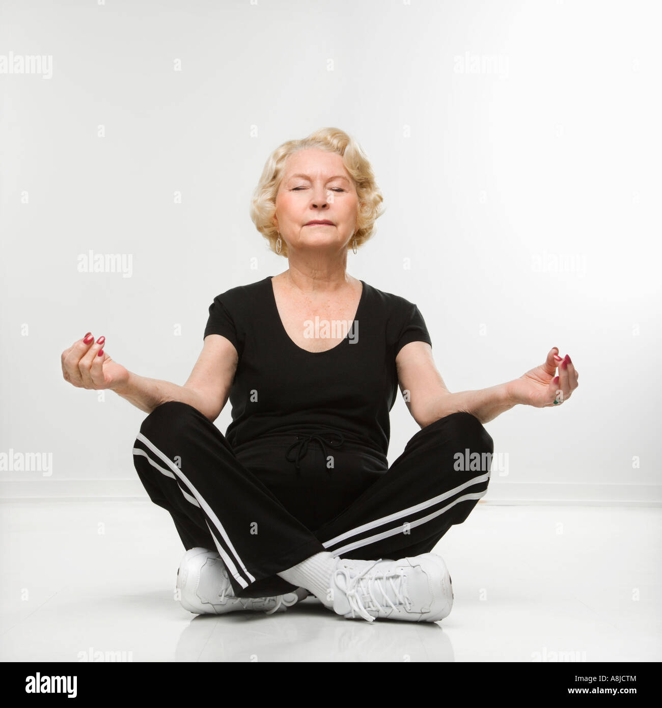 Caucasian senior woman sitting in yoga position on floor meditating ...