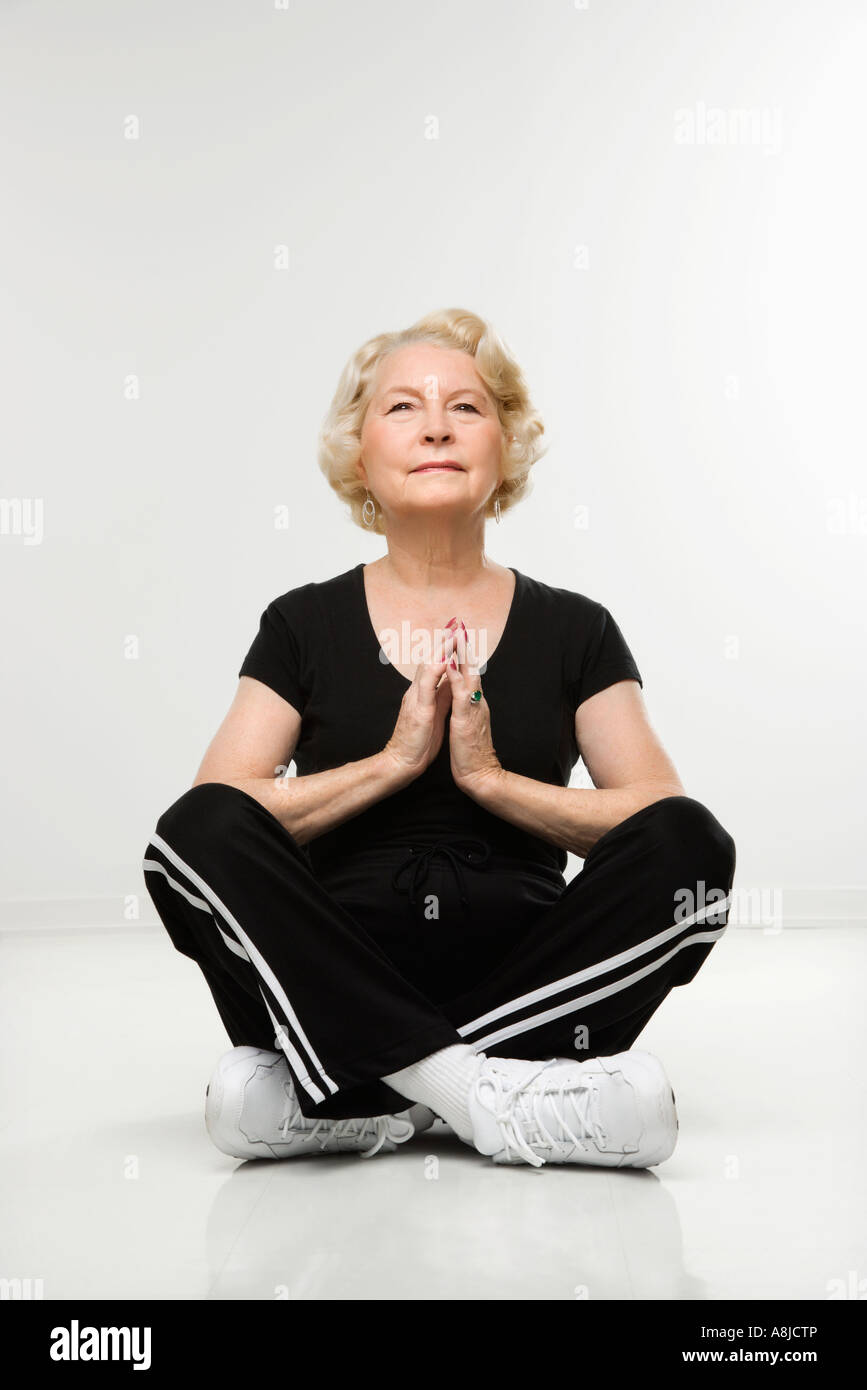 Caucasian senior woman sitting in yoga position on floor meditating ...