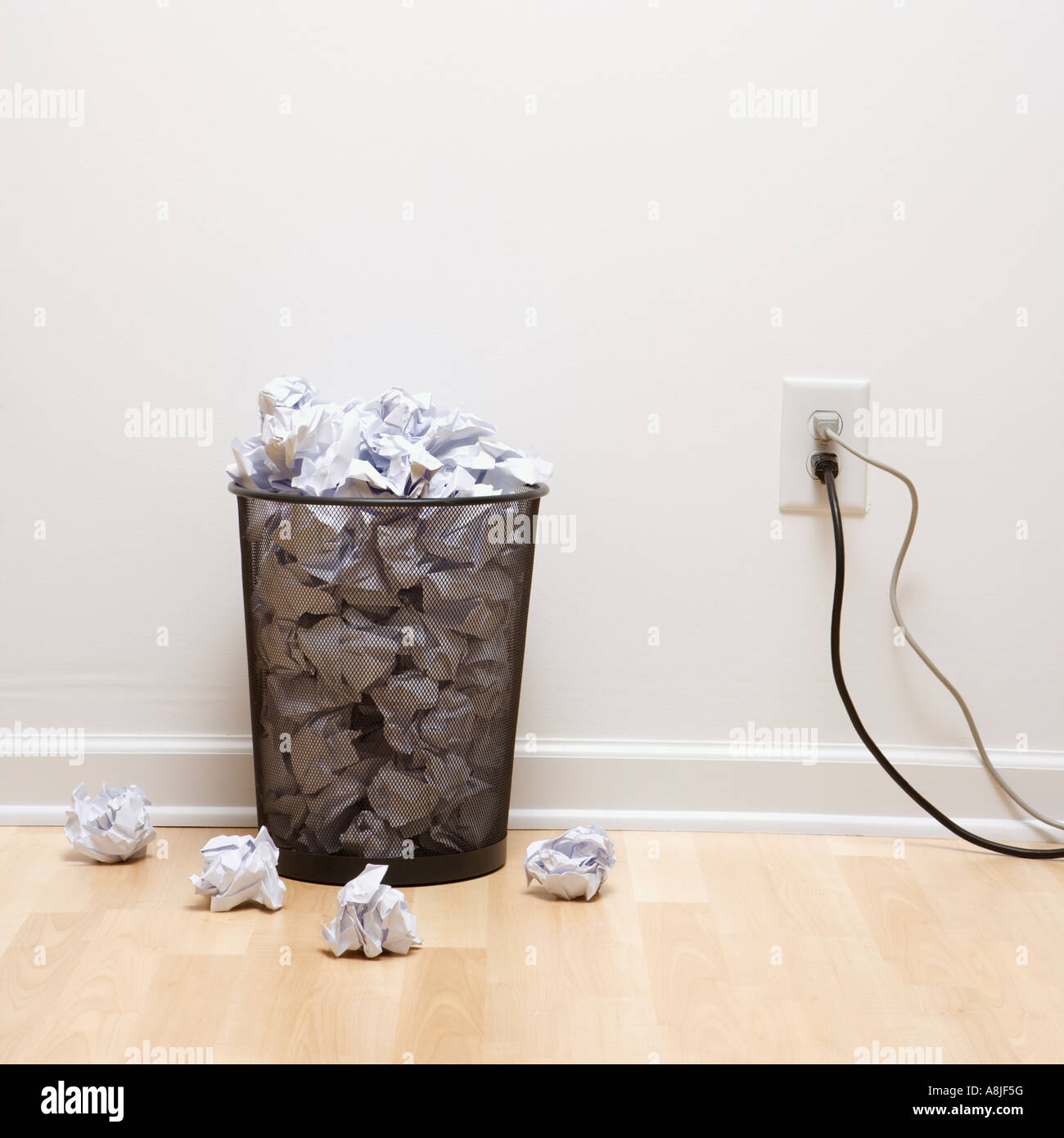 Full wire mesh trash can with crumpled paper next to electrical outlet