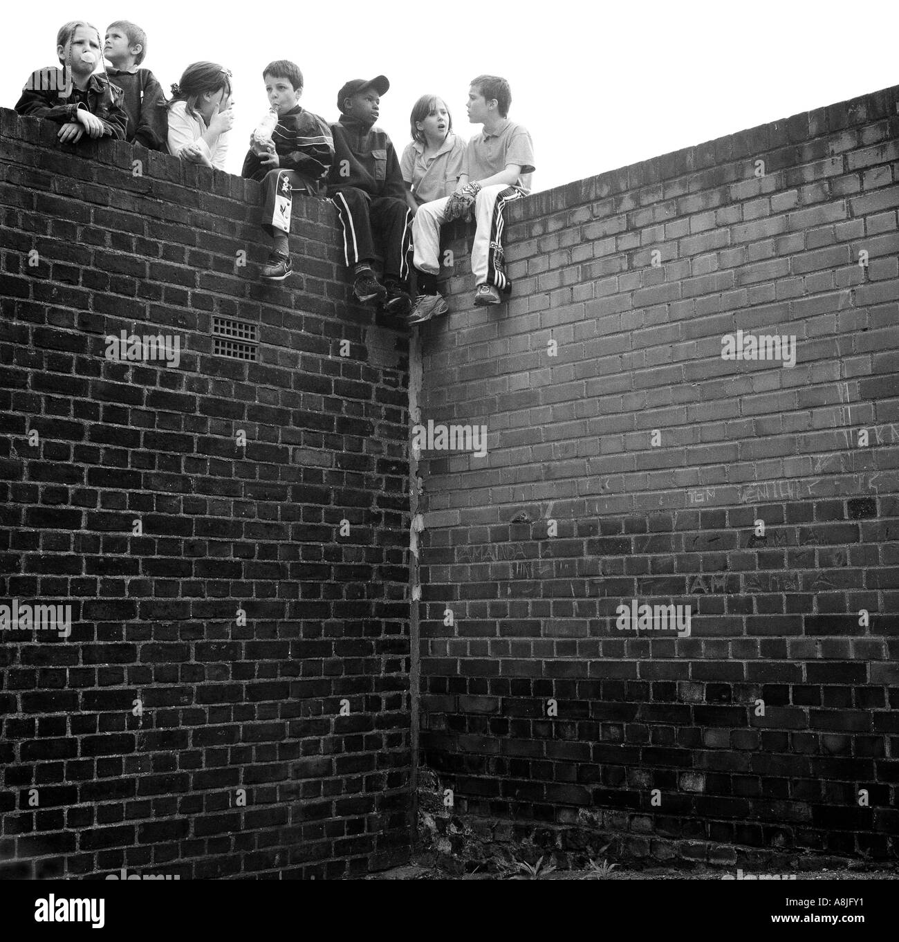 Children sitting on a brick wall on their housing estate, Clapton, London, UK. Stock Photo