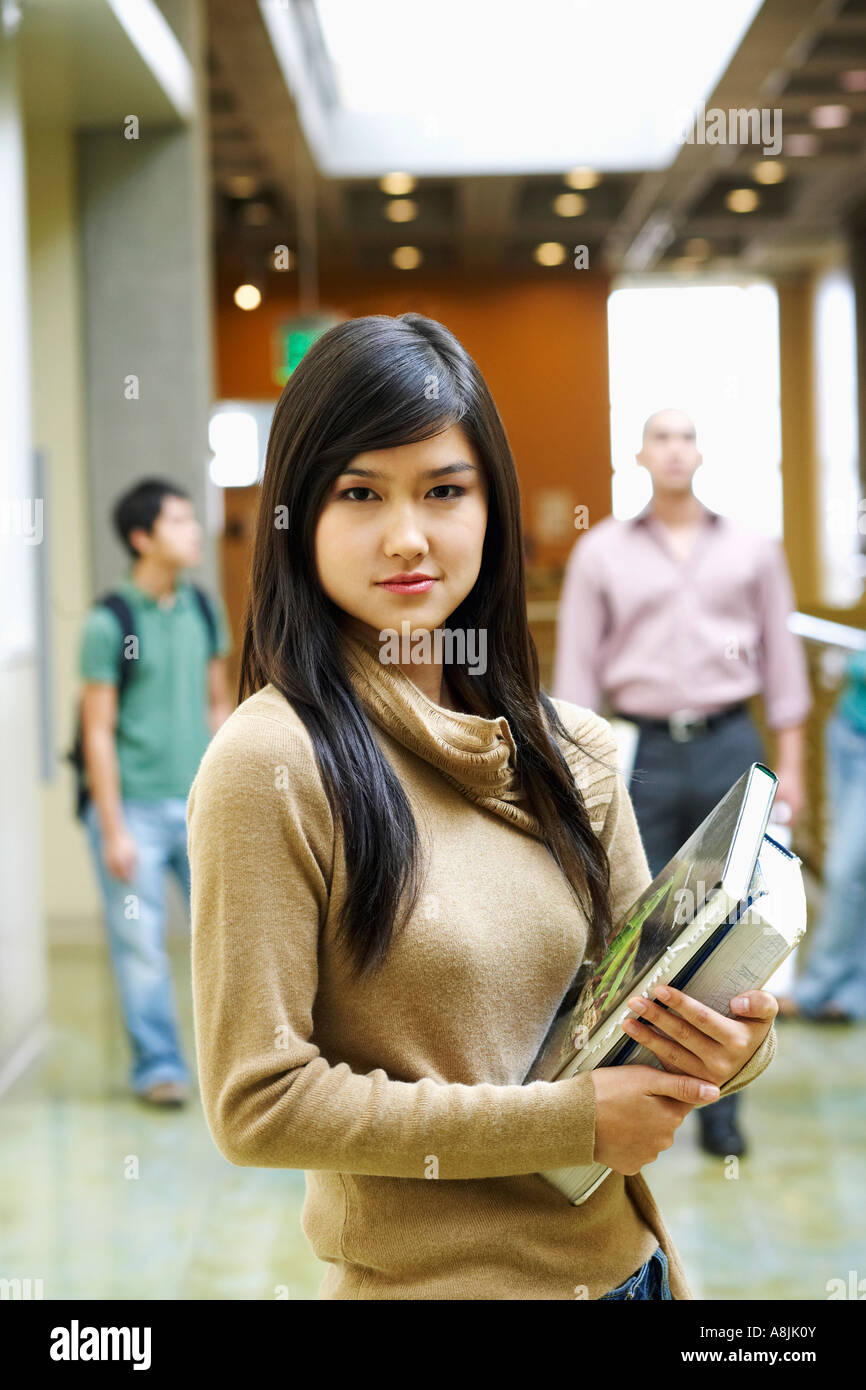 Portrait of a young woman holding books and standing in the corridor ...