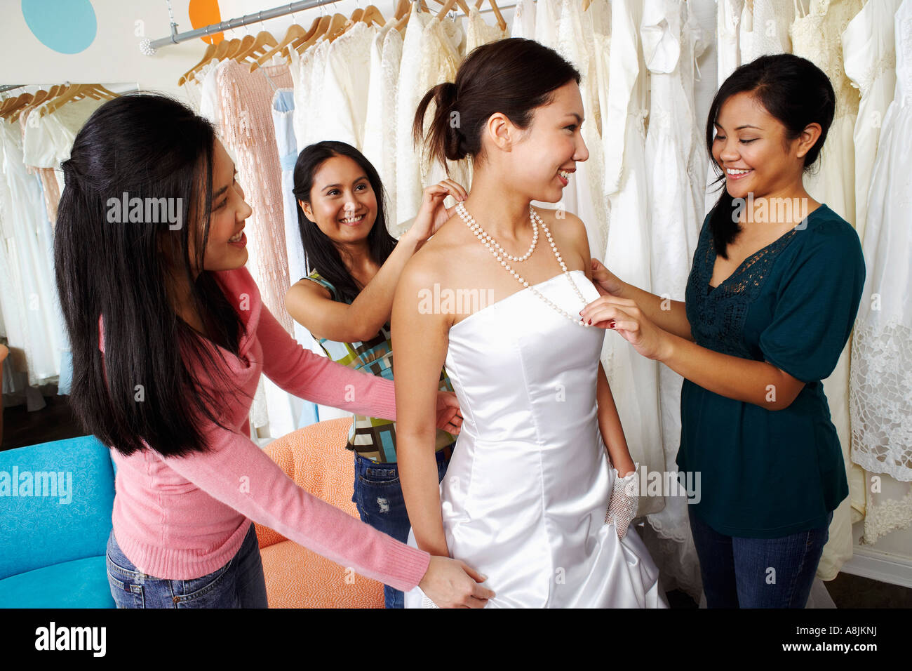 Three young women helping their friend try on a wedding dress in a ...
