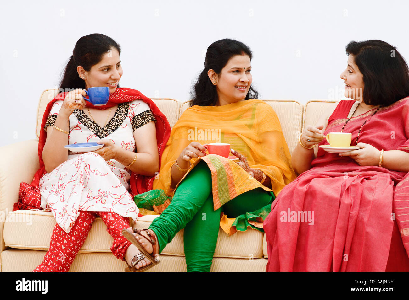Two mid adult women and a mature woman sitting on a couch and gossiping ...