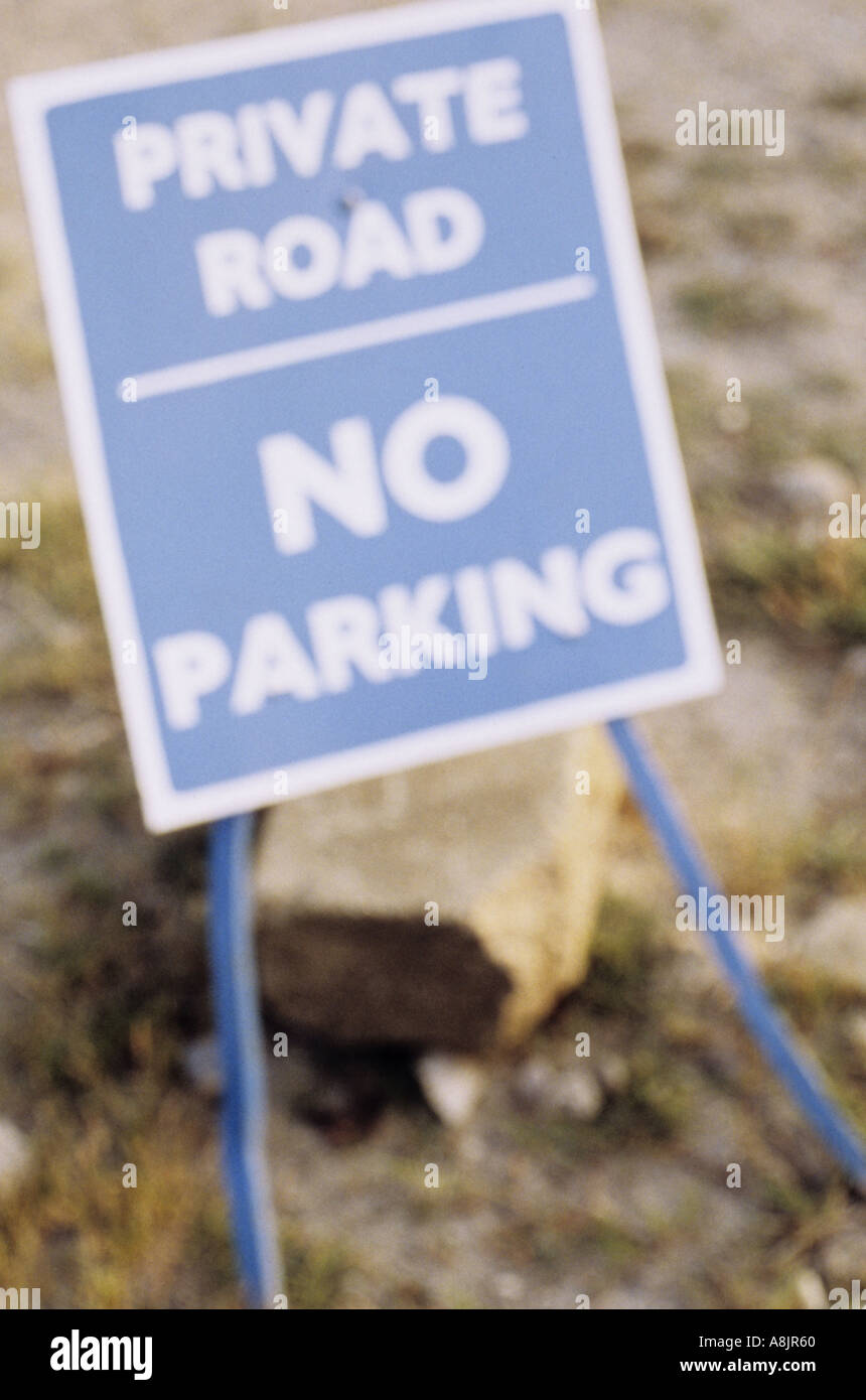 Defocussed sign on spindly legs and supported by a stone saying Private road No parking Stock Photo