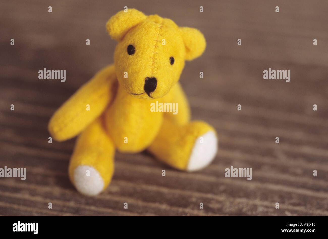 Small teddy bear sitting on a wooden seat or table Stock Photo