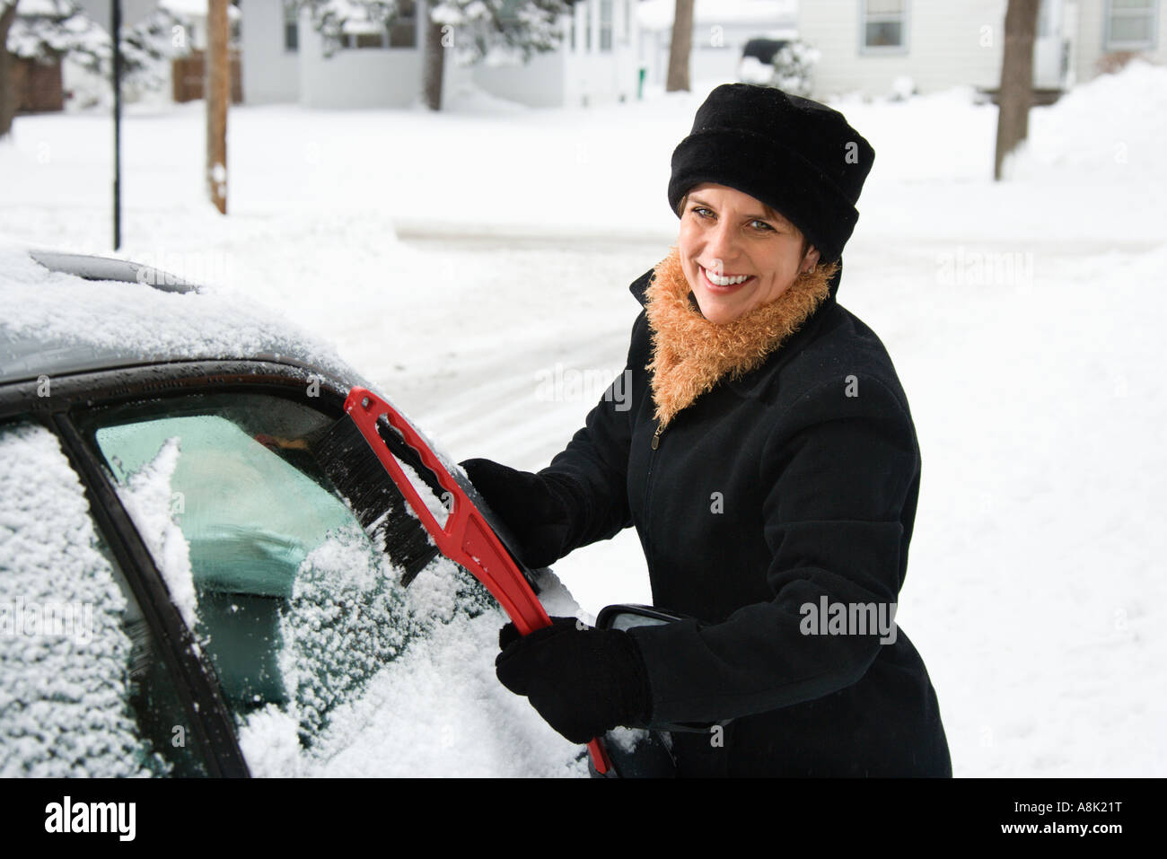 Caucasian mid adult woman scraping ice off car windshield and smiling