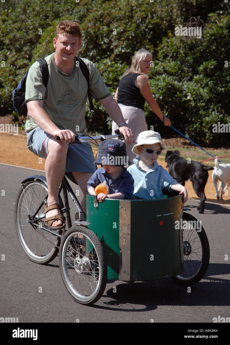 Father with two children in cart on T bike cycle in Dulwich Park london