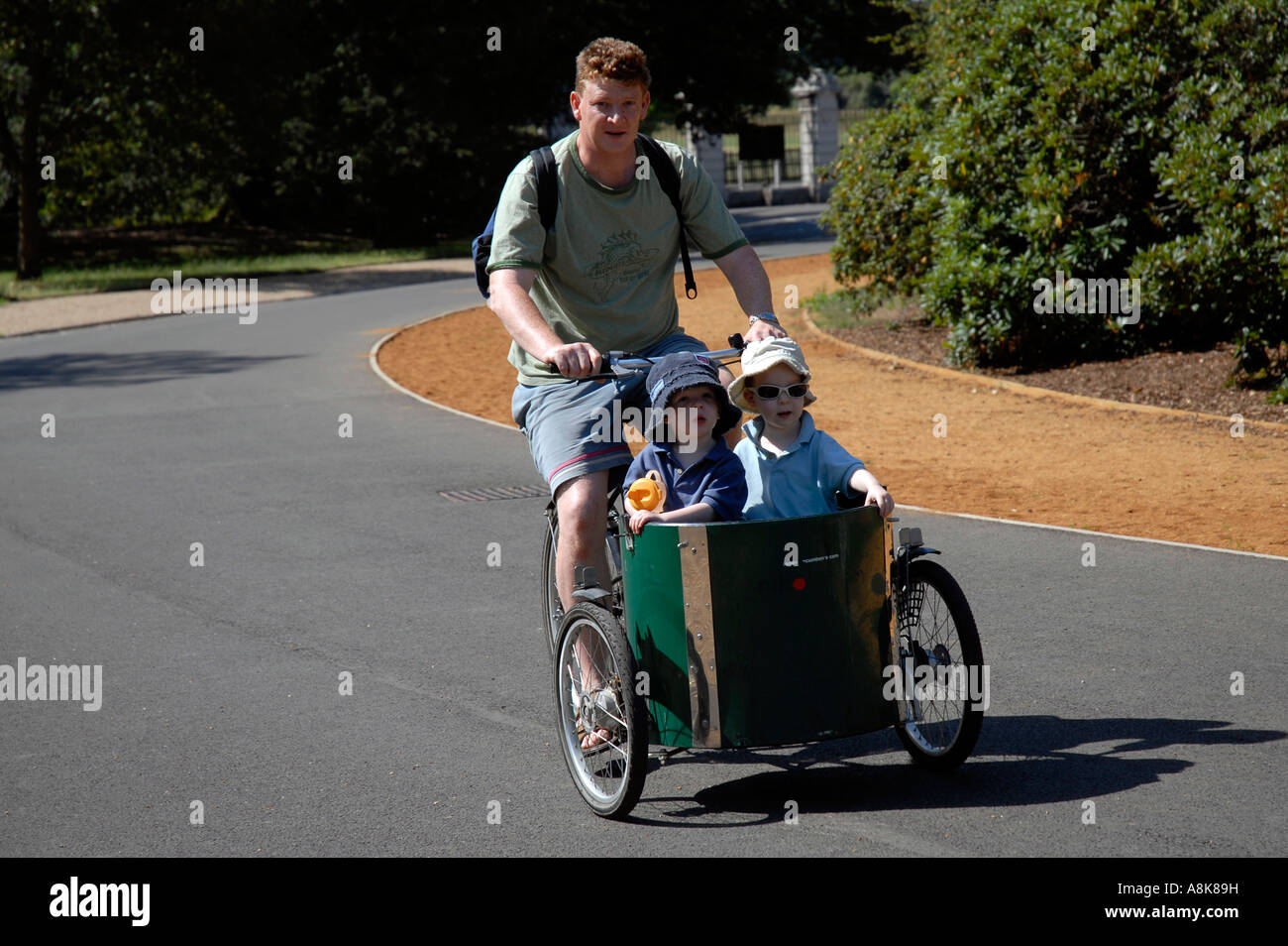 Father with two children in cart on T bike cycle in Dulwich Park london