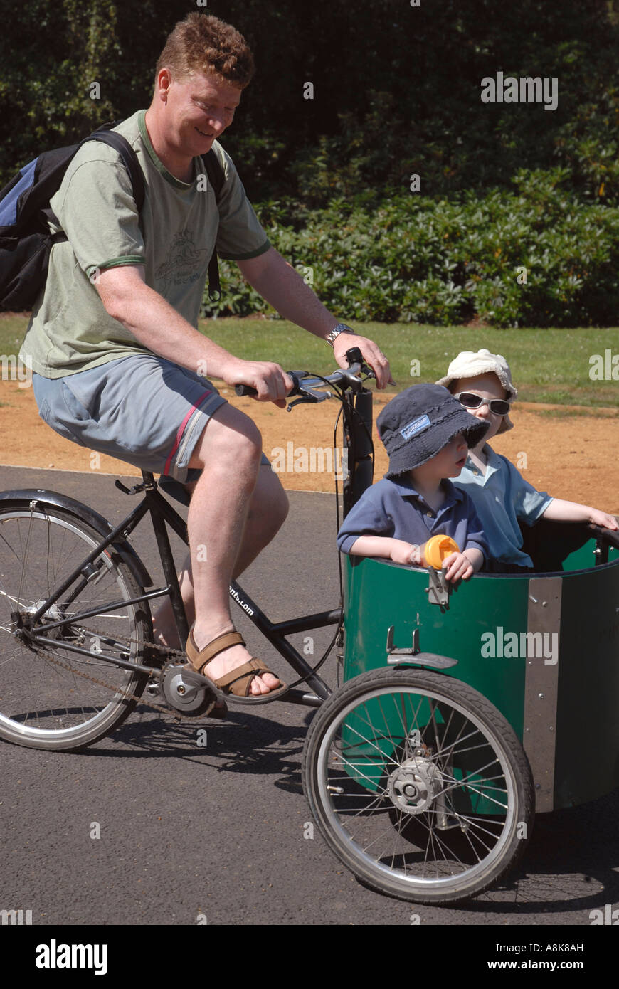 Father with two children in cart on T bike cycle in Dulwich Park london