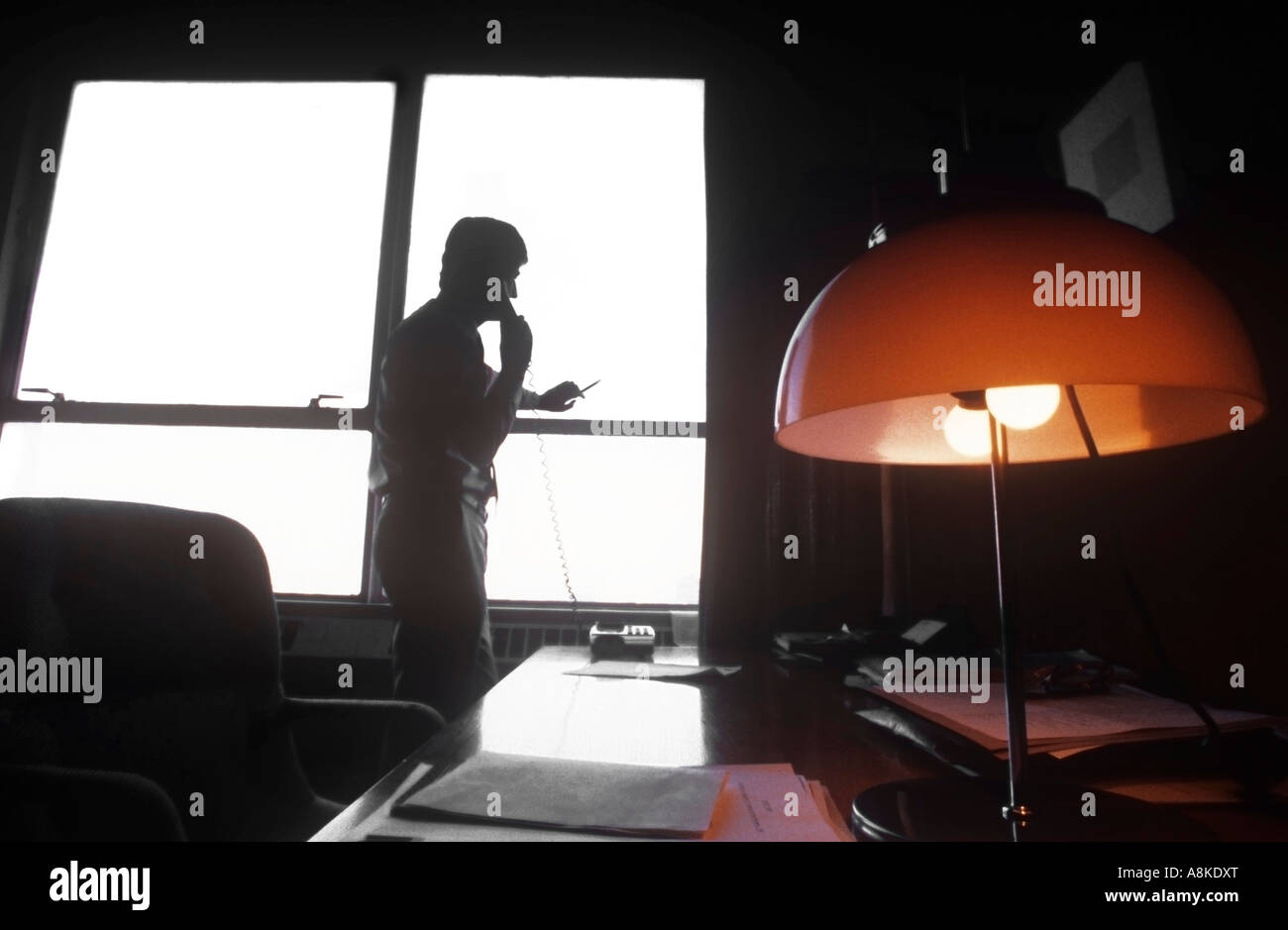 Executive man on corded telephone in 1980s office silhouetted against window. Stock Photo