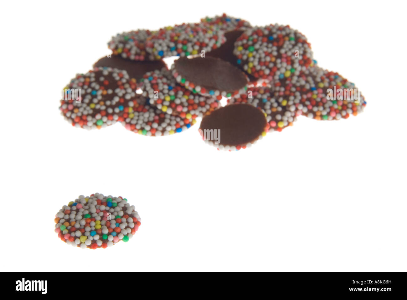 Horizontal close up of a pile of milk chocolate buttons on a white background. Stock Photo