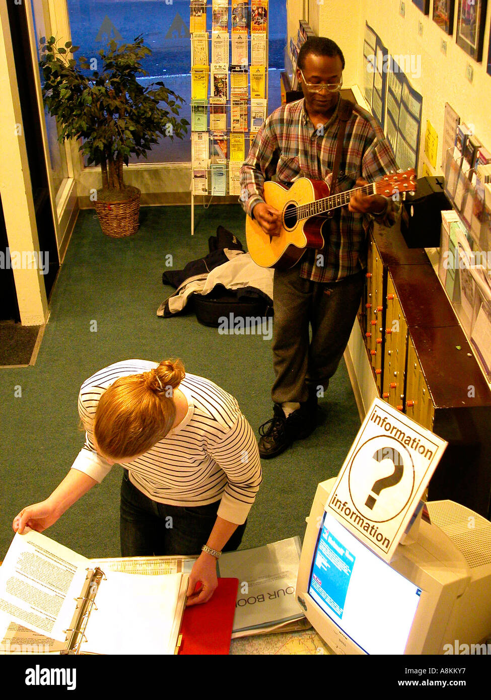 Student traveler getting information and a African American man playing a guitar at Mason Street youth hostel in San Francisco California Stock Photo