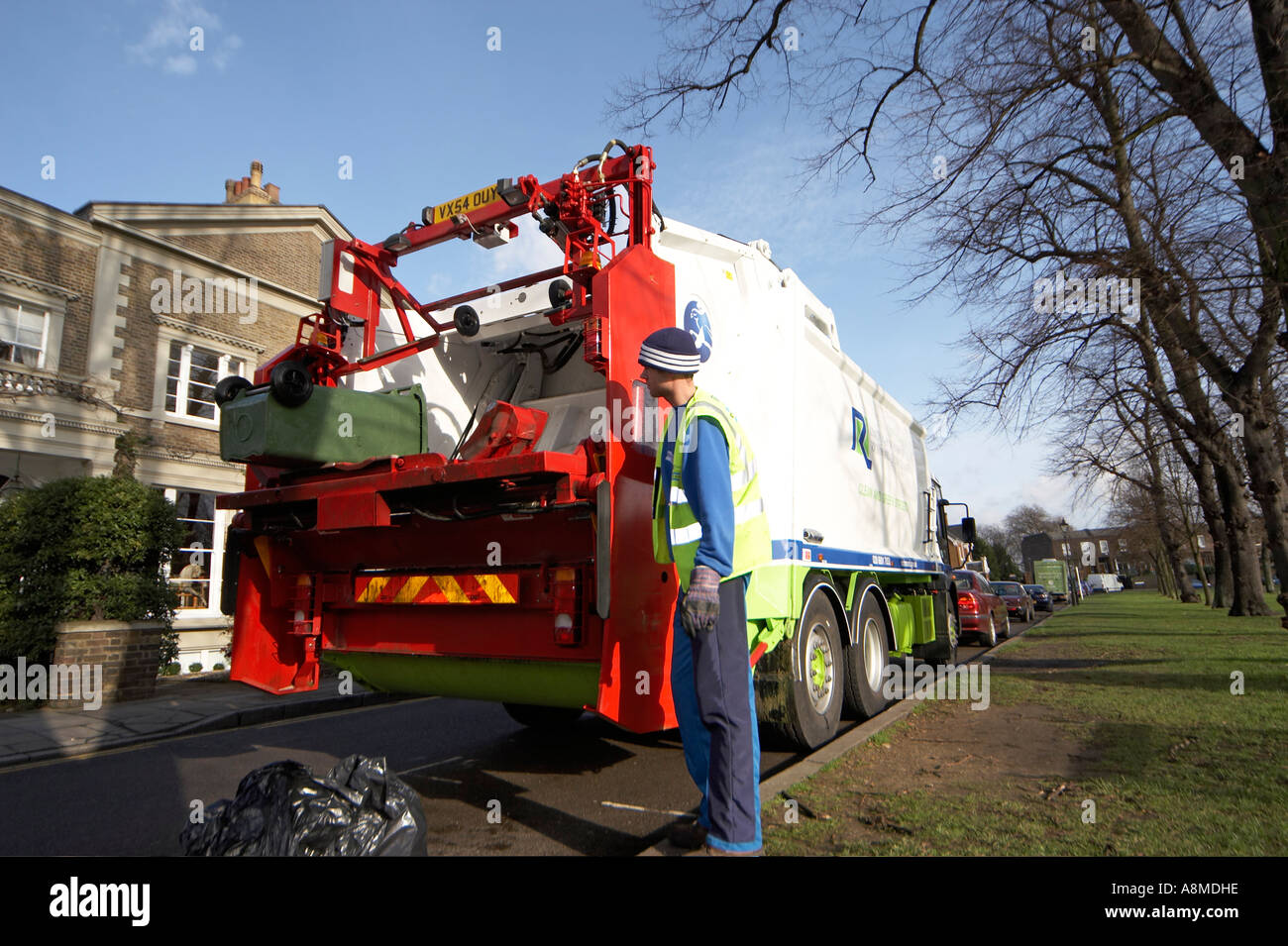 Waste rubbish or trash lorry or truck lifting green bin with man in