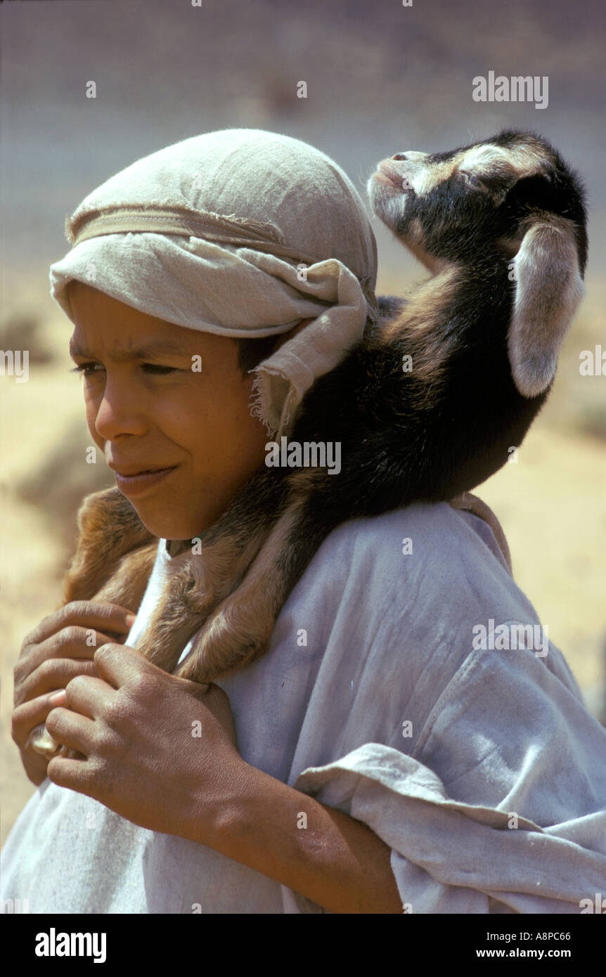 Young Arab boy carries a baby goat on his shoulders in Atlas mountains Morocco Stock Photo