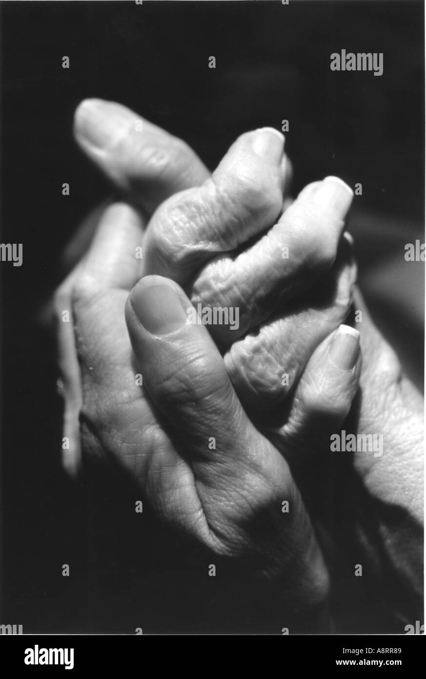 Close up of elderly arthritic hands being held by middle aged hands Black and white Stock Photo