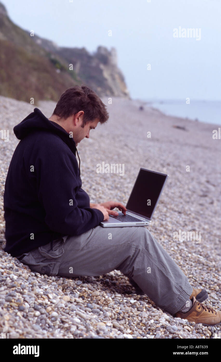 man beach laptop wireless work relax pebble devon Stock Photo