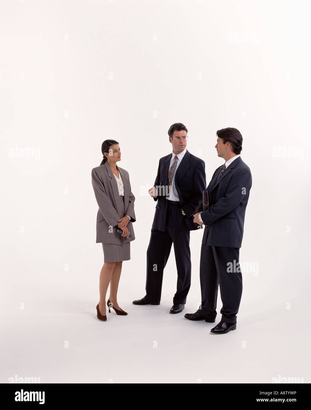 Group of three young people wearing business suits standing in studio on plain white background. Stock Photo