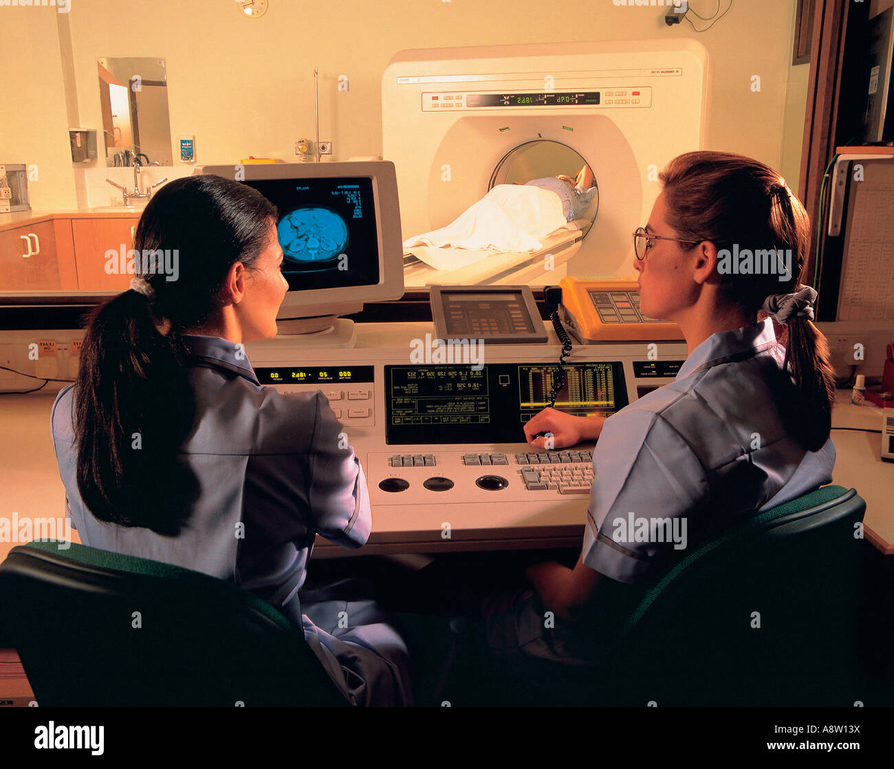 Young women hospital nurses at computerized controls of CT Scanning Computed Tomography unit. Stock Photo